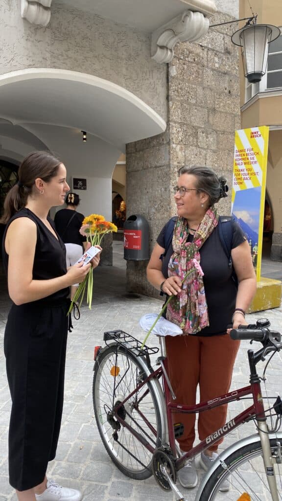  Standortleiterin Alina Priß mit Geburtagsblume und einer interessierten Passantin.